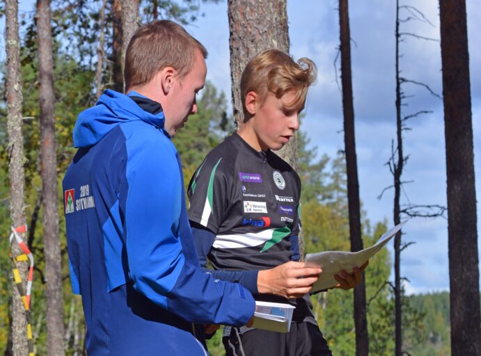 Suunnistusvalmentaja ja nuori suunnistaja katsovat karttaa järvimaisemassa.